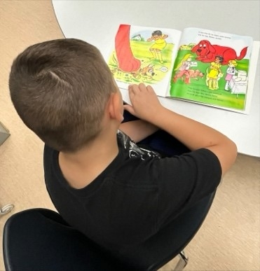 A child sitting at a table reading a book

Description automatically generated, Picture